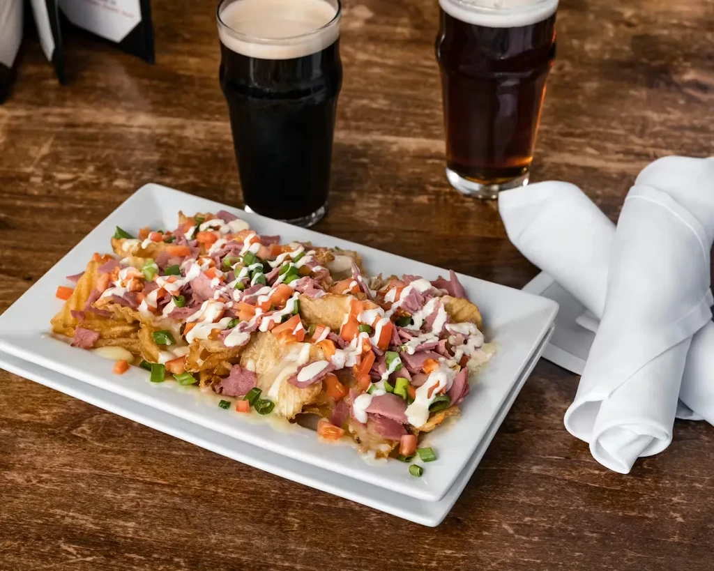 Loaded waffle fries with meat, tomatoes, sauce, and beer glasses.