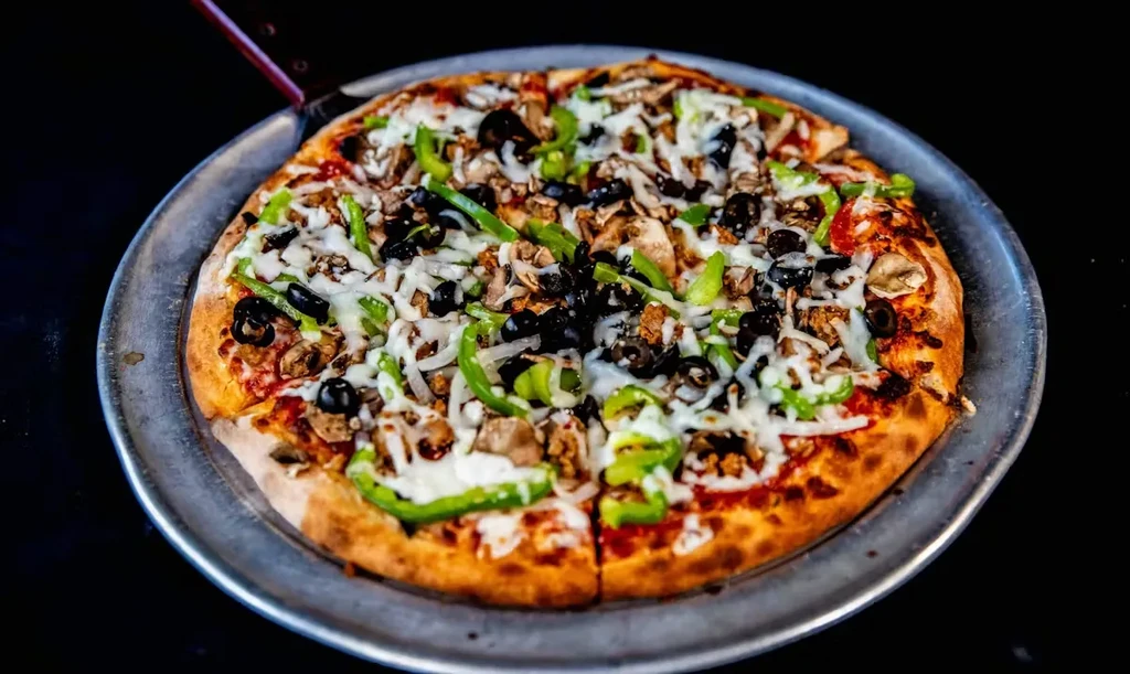 Sliced pizza with mozzarella, bell peppers, olives, mushrooms, meat on silver pan.
