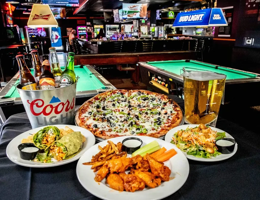 Pizza, wings, salad, and beer on a table in a pool hall.