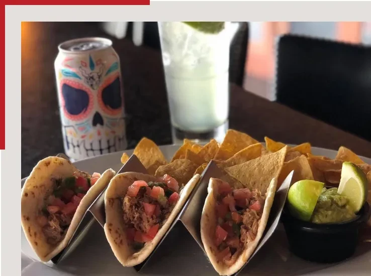 Close-up of three tacos, chips, and guacamole with lime.