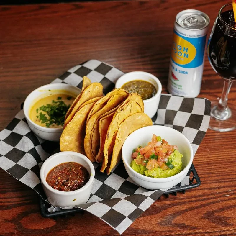 Basket of hard-shell tacos with four dips and two drinks.