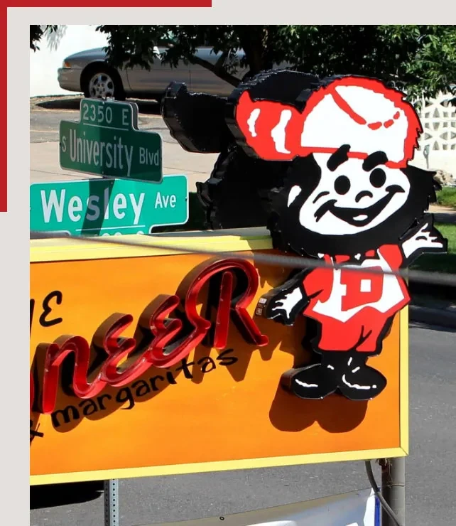 Outdoor sign for Pioneer Margaritas with cartoon mascot and street signs.