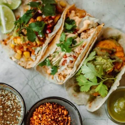 Overhead view of three loaded tacos with lime and bowls of toppings.