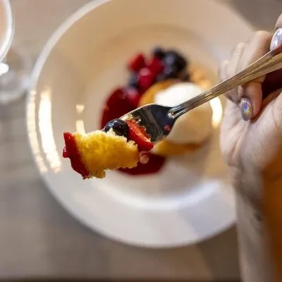 A fork lifts cake with red berry sauce and fresh berries.