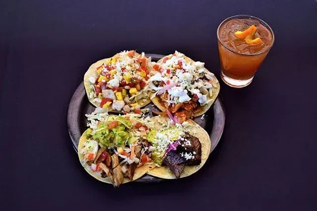 Overhead of four colorful, varied tacos and an amber drink.