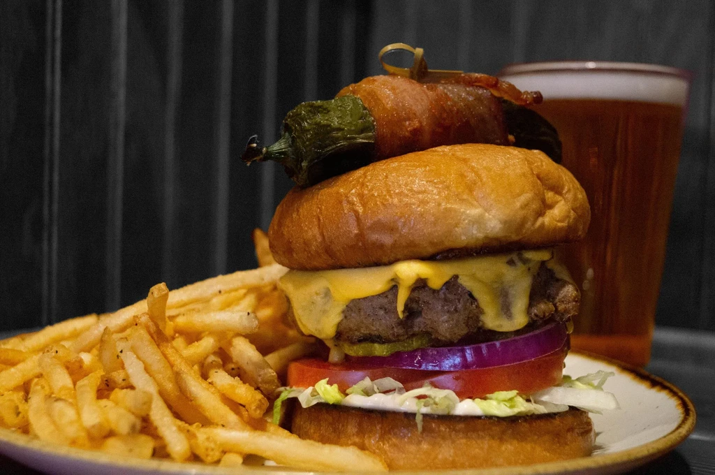 Close-up: Cheeseburger with bacon-wrapped jalapeño, fries, and beer.