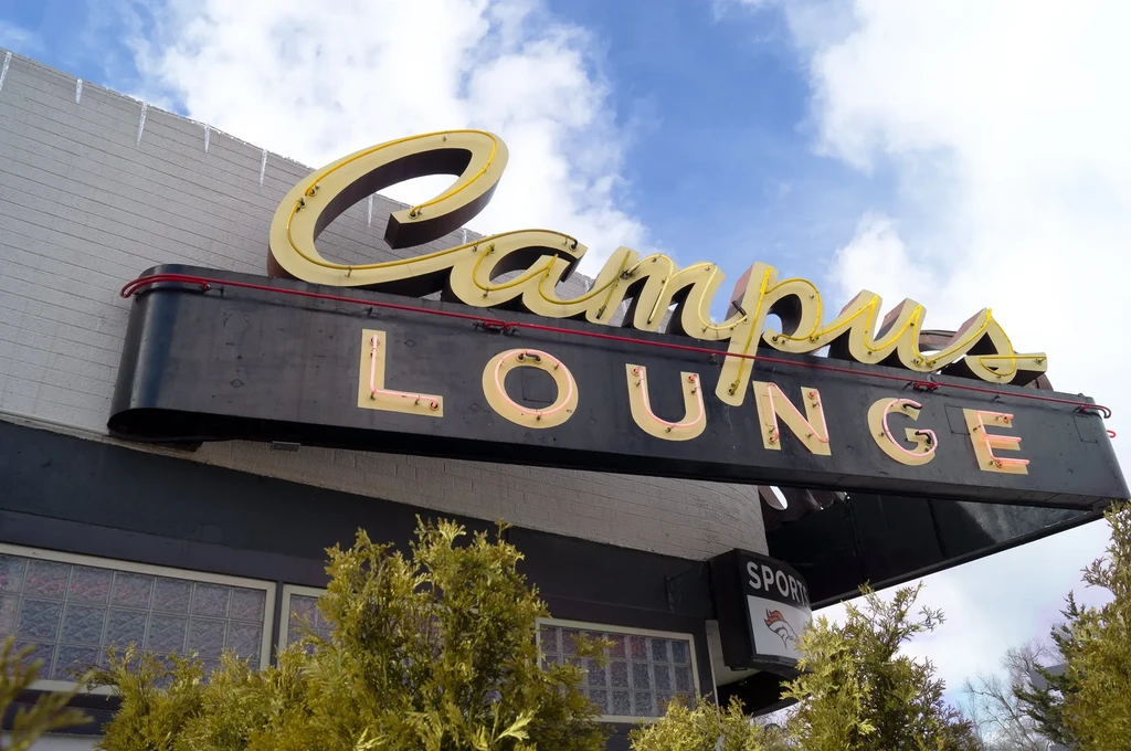 Classic gold neon 'Campus Lounge' sign on brick building with icicles.