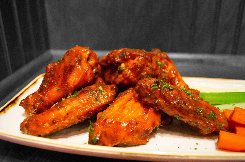 Plate of buffalo chicken wings with celery, carrots, and herbs.