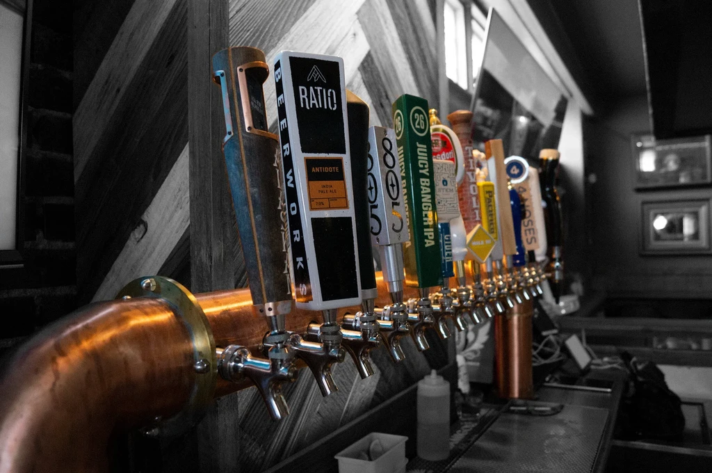 Close-up of a copper beer tap manifold with colorful branded handles.