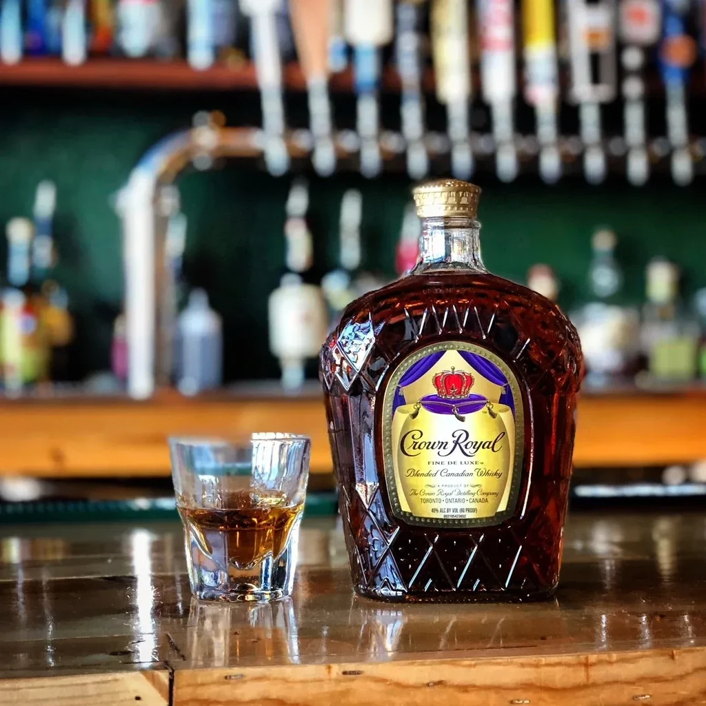 Crown Royal whisky bottle and shot glass on a wooden bar.