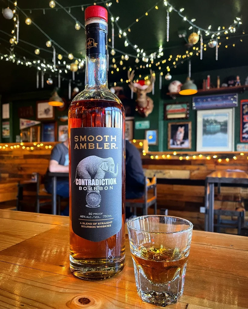 Smooth Ambler Contradiction Bourbon bottle and glass in a festive bar.