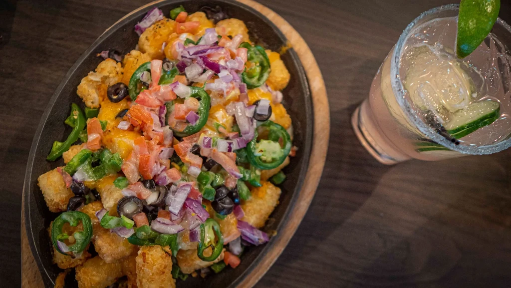 Overhead shot of loaded totchos in a skillet and a pink cocktail.