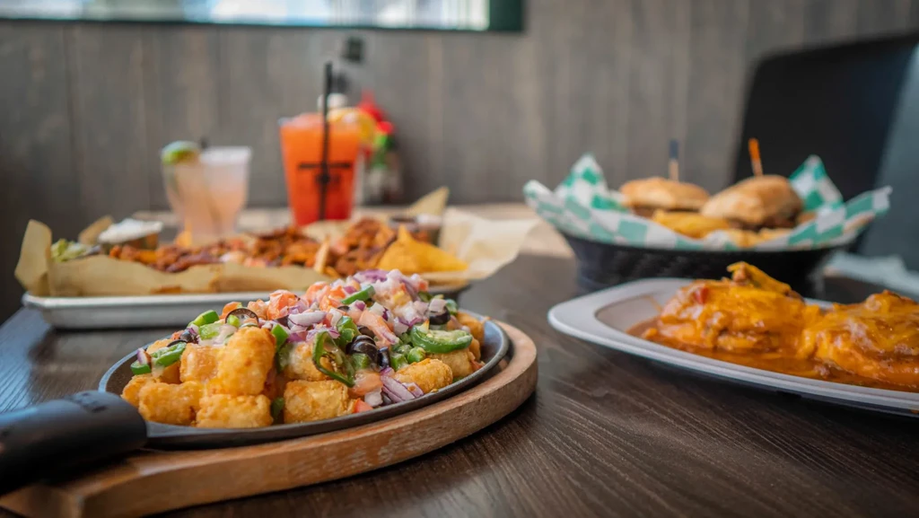 Sizzling loaded tater tots in skillet with various food and drinks.