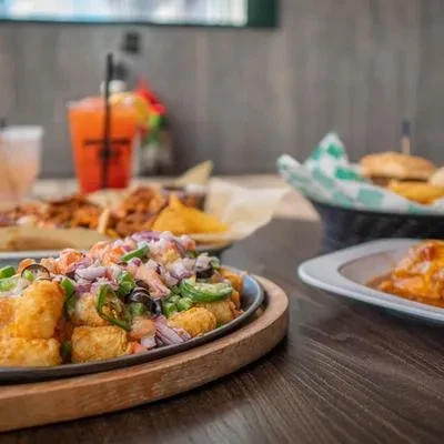 Sizzling tater tots with toppings, orange drink, and burger on a table.