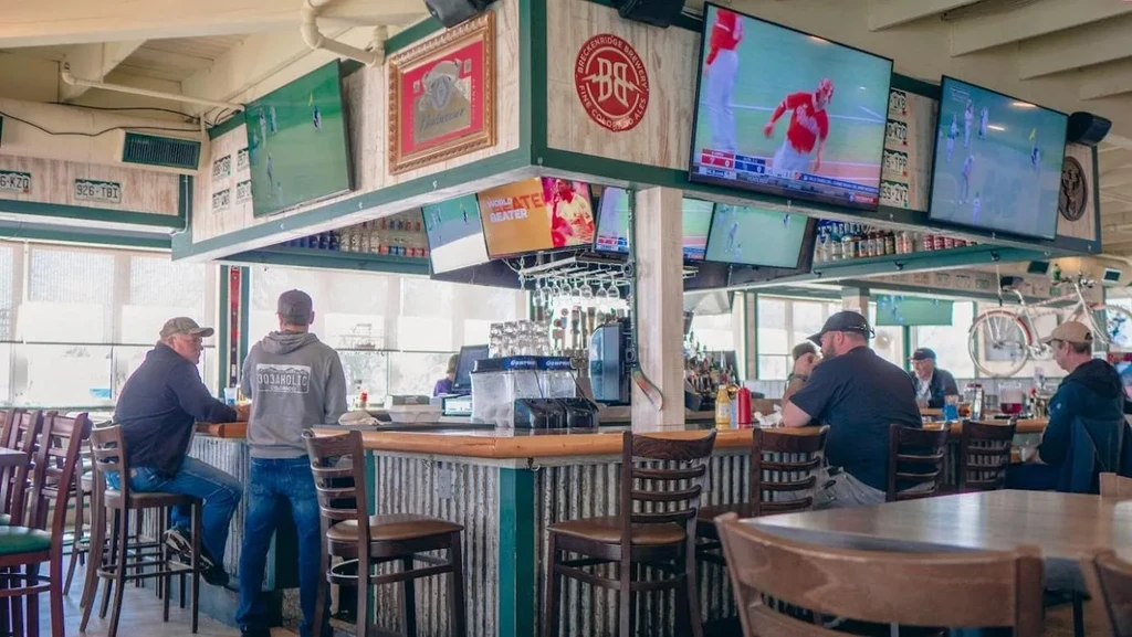 Men at a sports bar with rustic decor and multiple TVs.