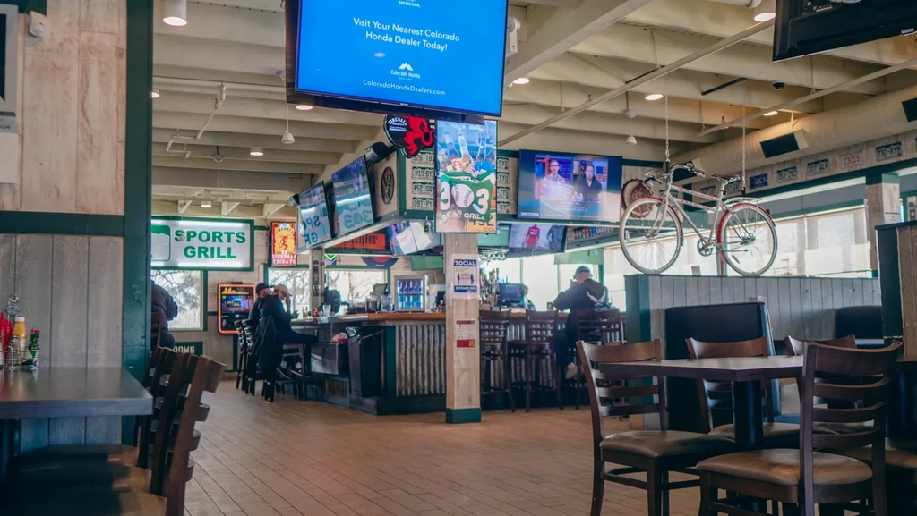Sports bar interior with a bar, many TVs, and empty tables.