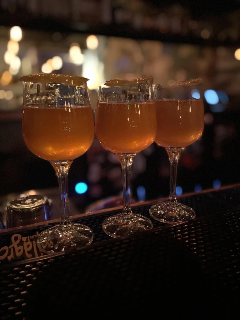 Three amber cocktails with fruit garnish on a dim bar top.