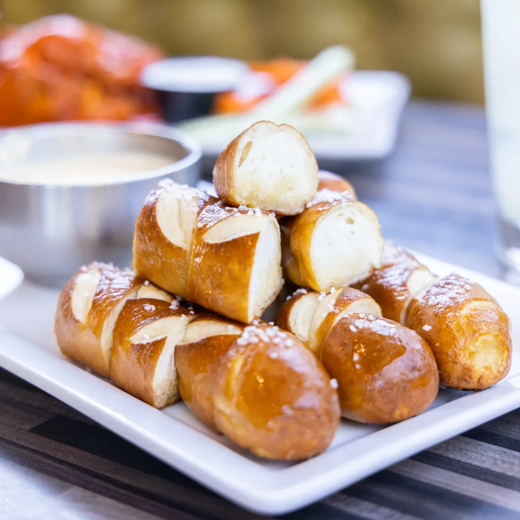 Golden pretzel bites, some halved, with salt and creamy dipping sauce.