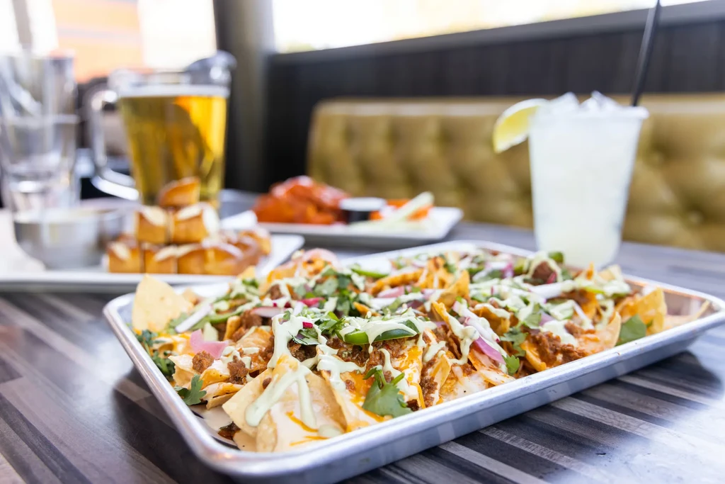 Close-up of loaded nachos with meat, cheese, green sauce, and cilantro.