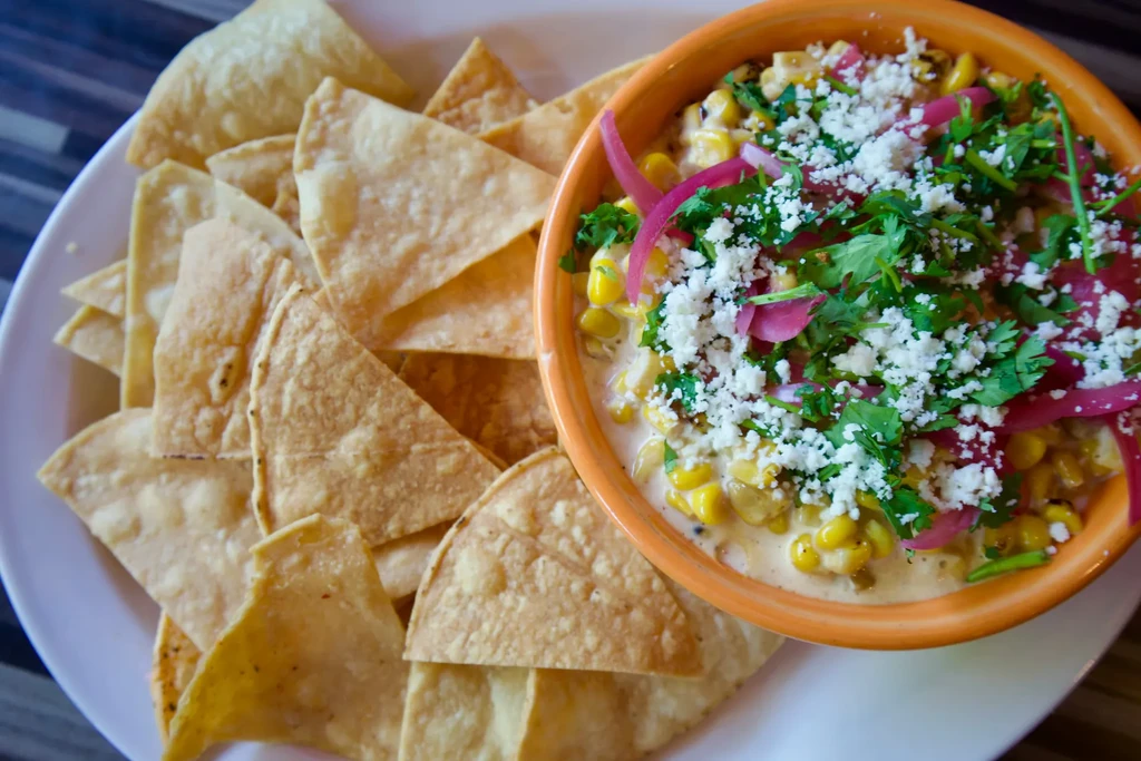 Orange bowl with creamy corn, cheese, cilantro, and chips.