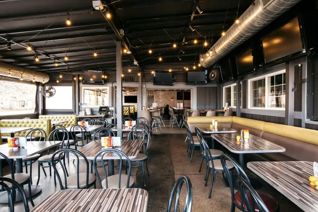 Empty casual dining room with tables, colorful booths, and wall-mounted TVs.