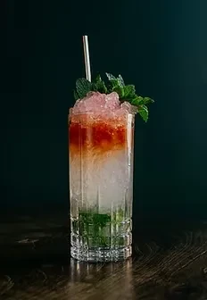 Layered green, clear, orange cocktail with crushed ice, mint, and straw.