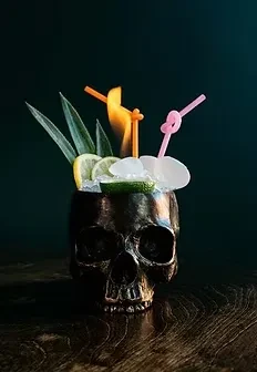 Flaming cocktail in a black skull mug, garnished with fruit and leaves.