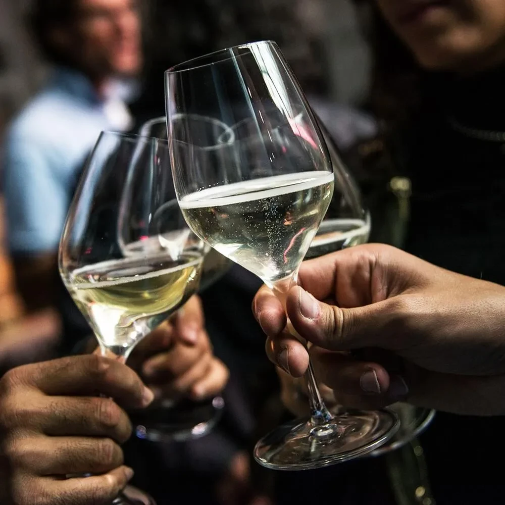 Close-up of hands holding sparkling wine glasses at a gathering.