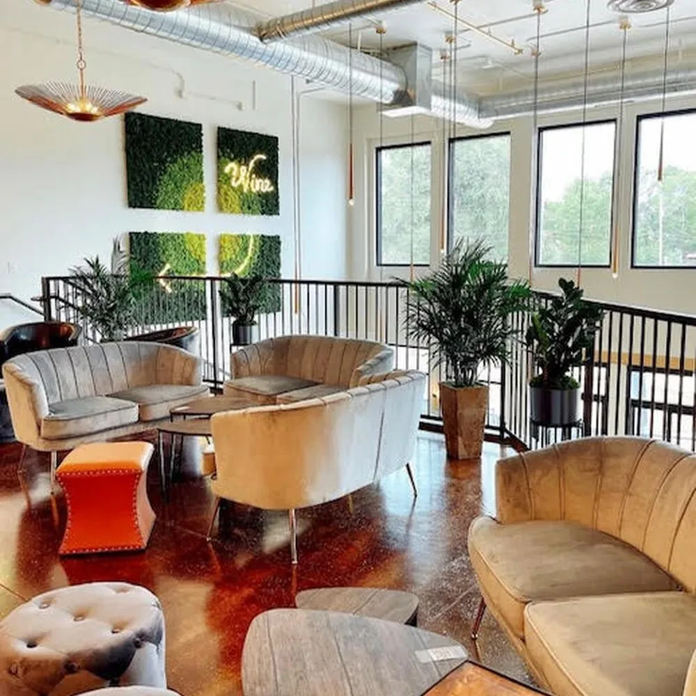 Modern lounge with velvet sofas, green moss art, and 'Wine' neon.