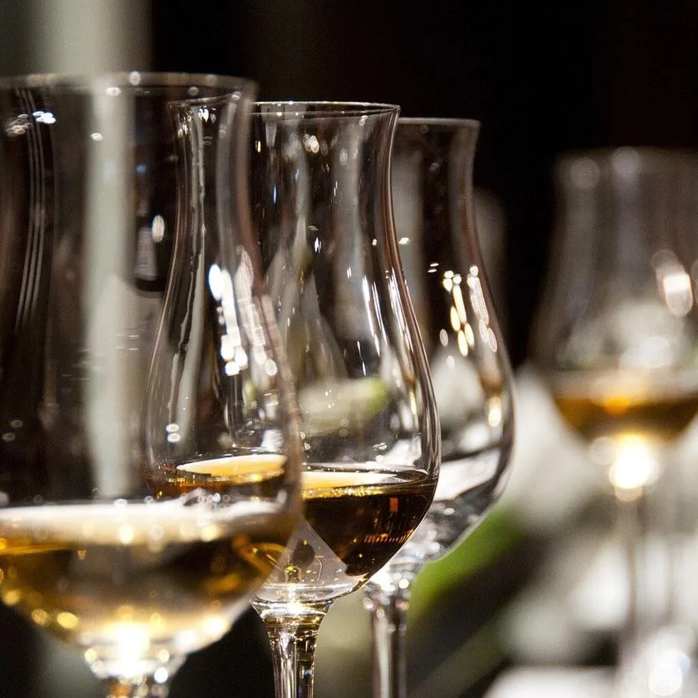 Row of stemmed glasses with amber liquid, the first in sharp focus.