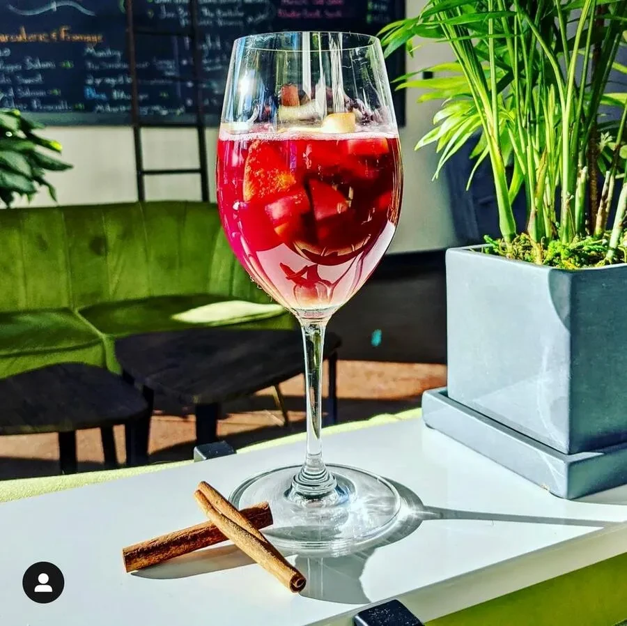 Wine glass with bubbly red fruit drink and two cinnamon sticks.