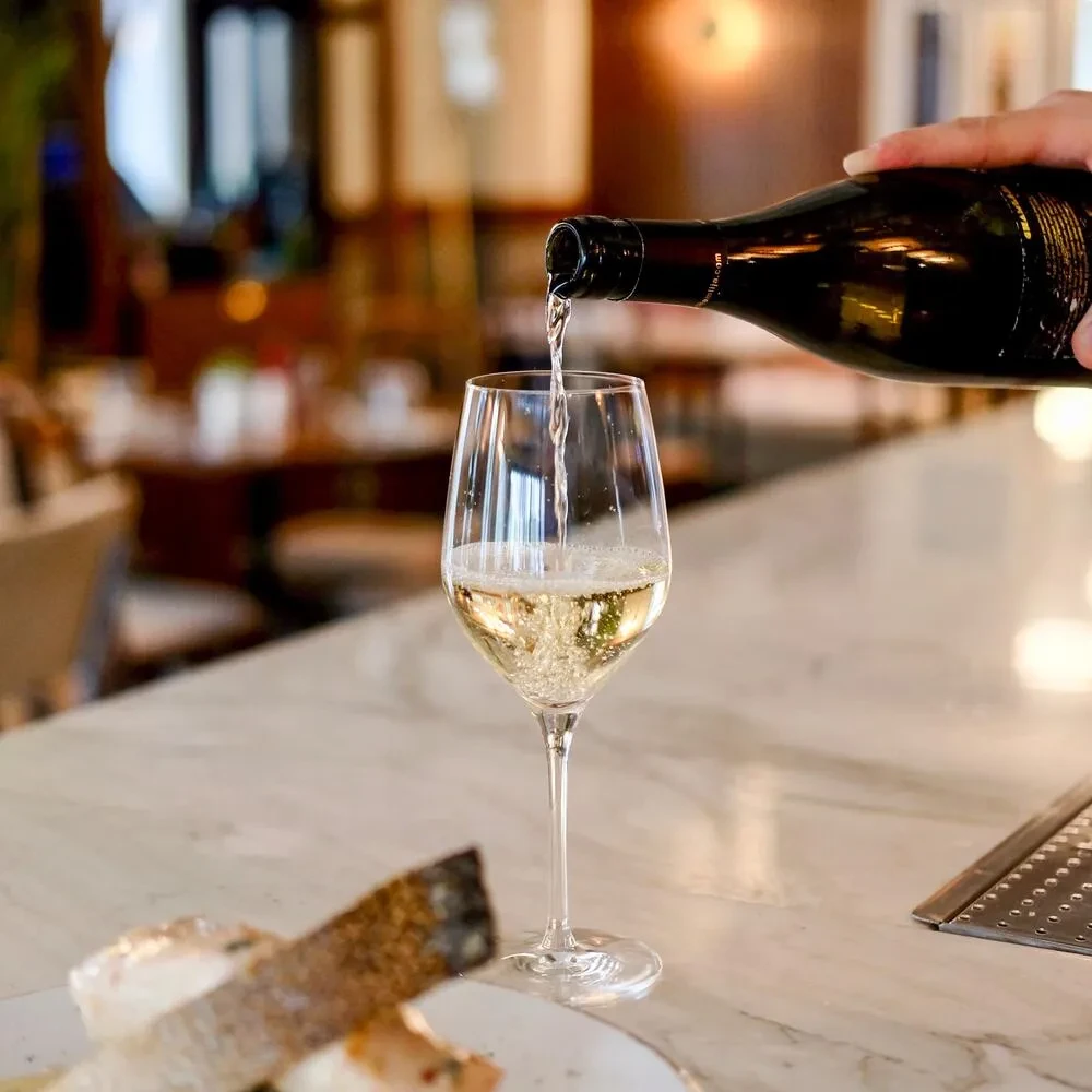 Sparkling wine actively pouring into a glass on a marble counter.