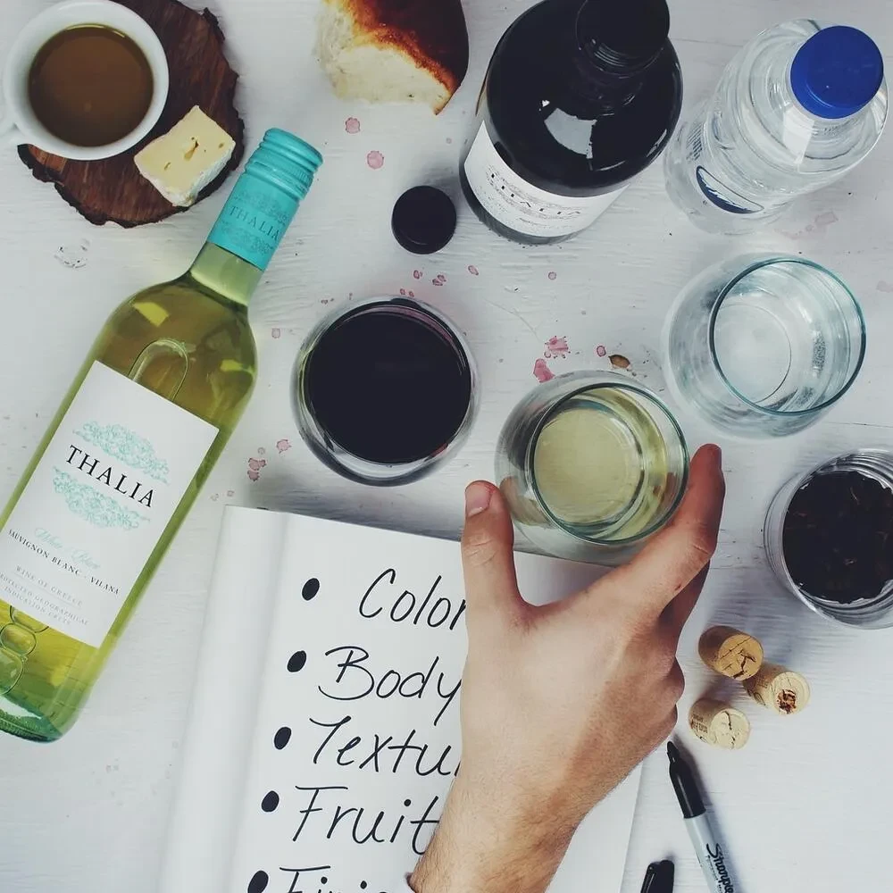 Overhead view of wine bottles, glasses, tasting notes, and a hand.