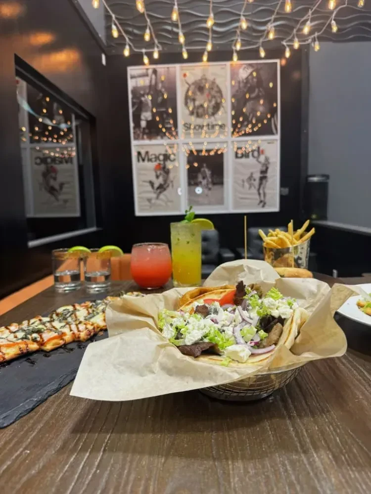 Flatbread pizza, gyro, fries, and cocktails on a dark restaurant table.