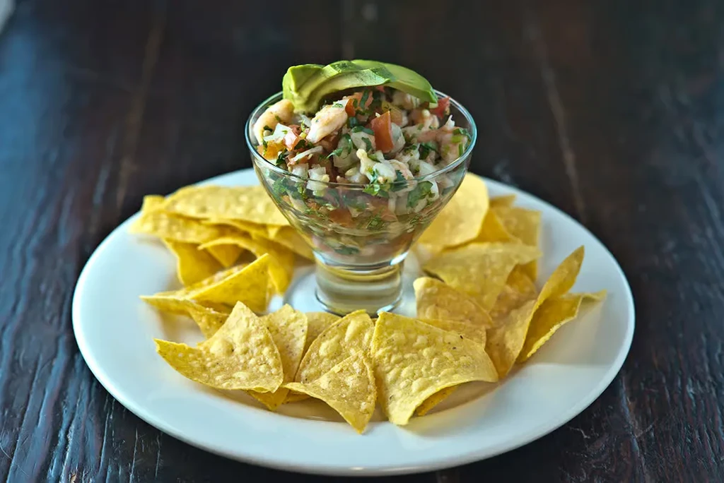 Ceviche in a glass dish, garnished with avocado, served with tortilla chips.
