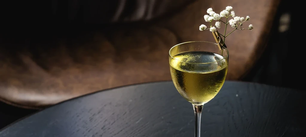 Clear yellowish-green cocktail in a coupe glass garnished with baby's breath.