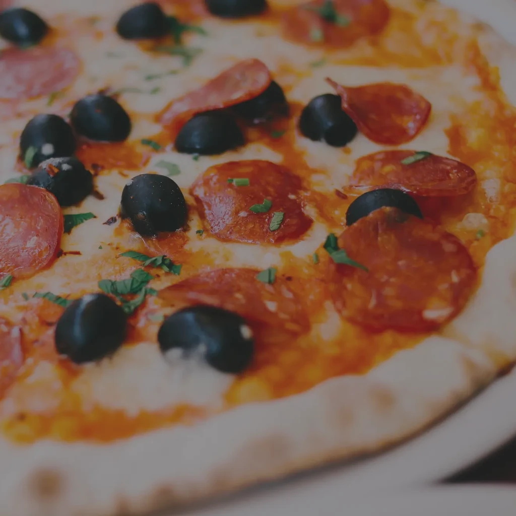 Baked pizza topped with pepperoni, black olives, cheese, and herbs.