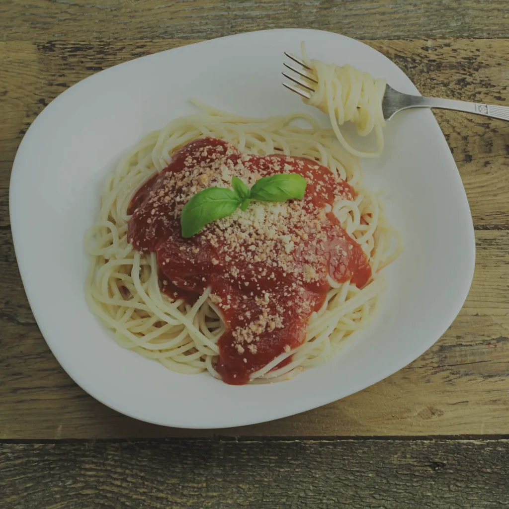 Spaghetti with tomato sauce, cheese, basil, and a fork on a rustic table.