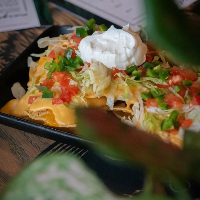 Close-up of cheesy nachos with sour cream and fresh vegetables.