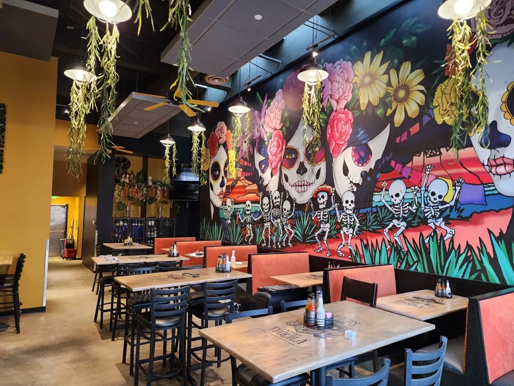 Vibrant restaurant interior with Dia de los Muertos mural, booths, and plants.