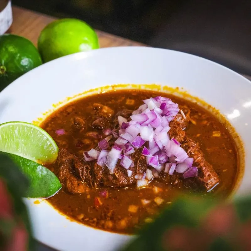 Hearty meat stew with red onions and lime wedges in a white bowl.