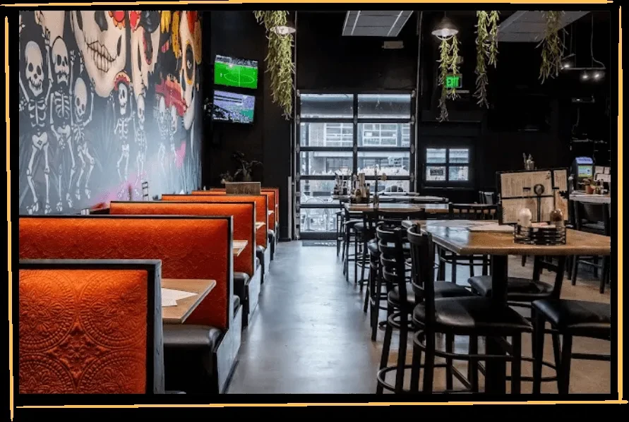 Restaurant interior with orange booths, high-top tables, and Dia de los Muertos mural.
