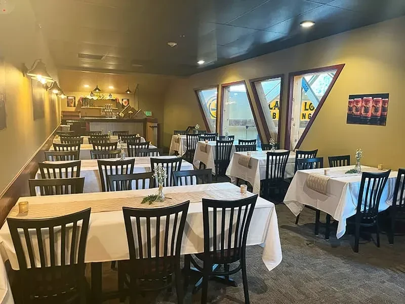 Empty restaurant dining room with set tables, bar, and unique windows.