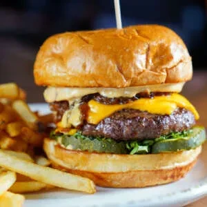 Gourmet burger with melted cheese, pickles, and hand-cut fries.