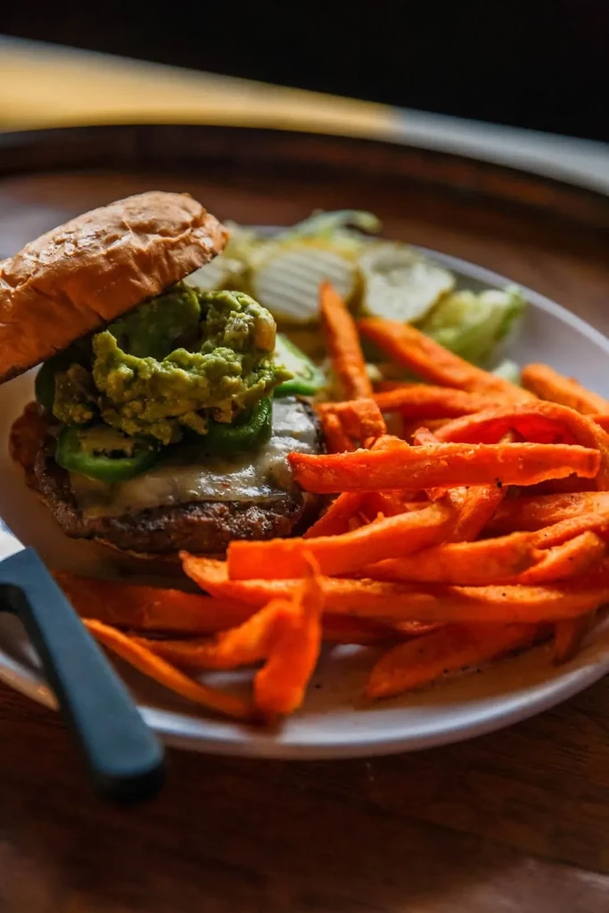 Gourmet burger with guacamole, jalapeños, sweet potato fries, and salad.
