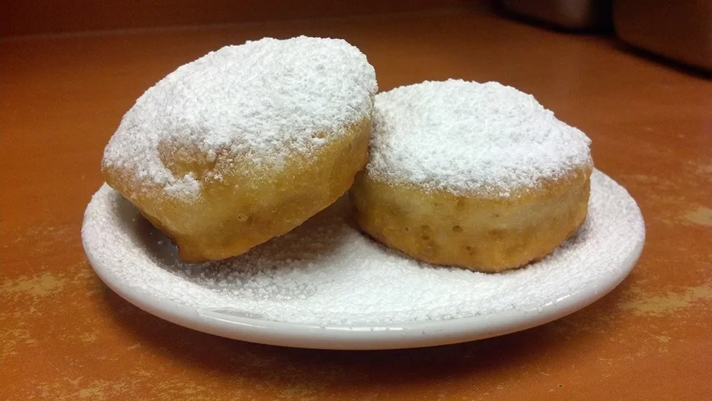 Two golden fried pastries with white powdered sugar on a white plate.