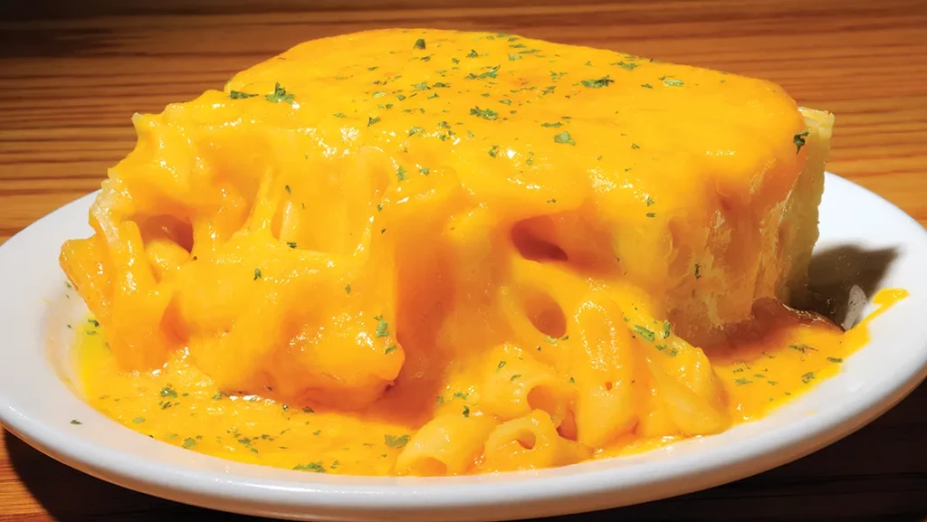 Close-up rectangular macaroni and cheese with melted cheese and green herbs.