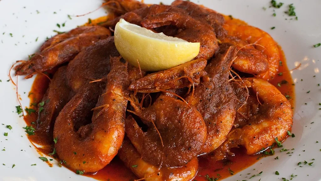 Large whole shrimp in reddish-brown sauce with lemon and green herbs.