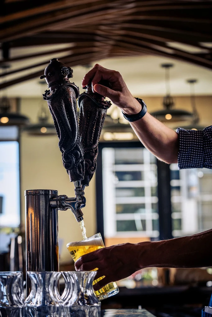 Hand pulls ornate tap, pouring golden beer into glass.