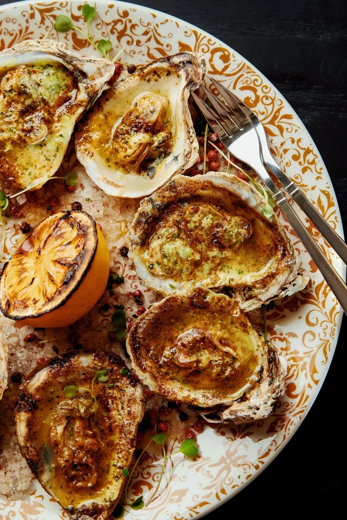 Baked oysters with herb butter sauce, lemon, pink peppercorns, and greens.
